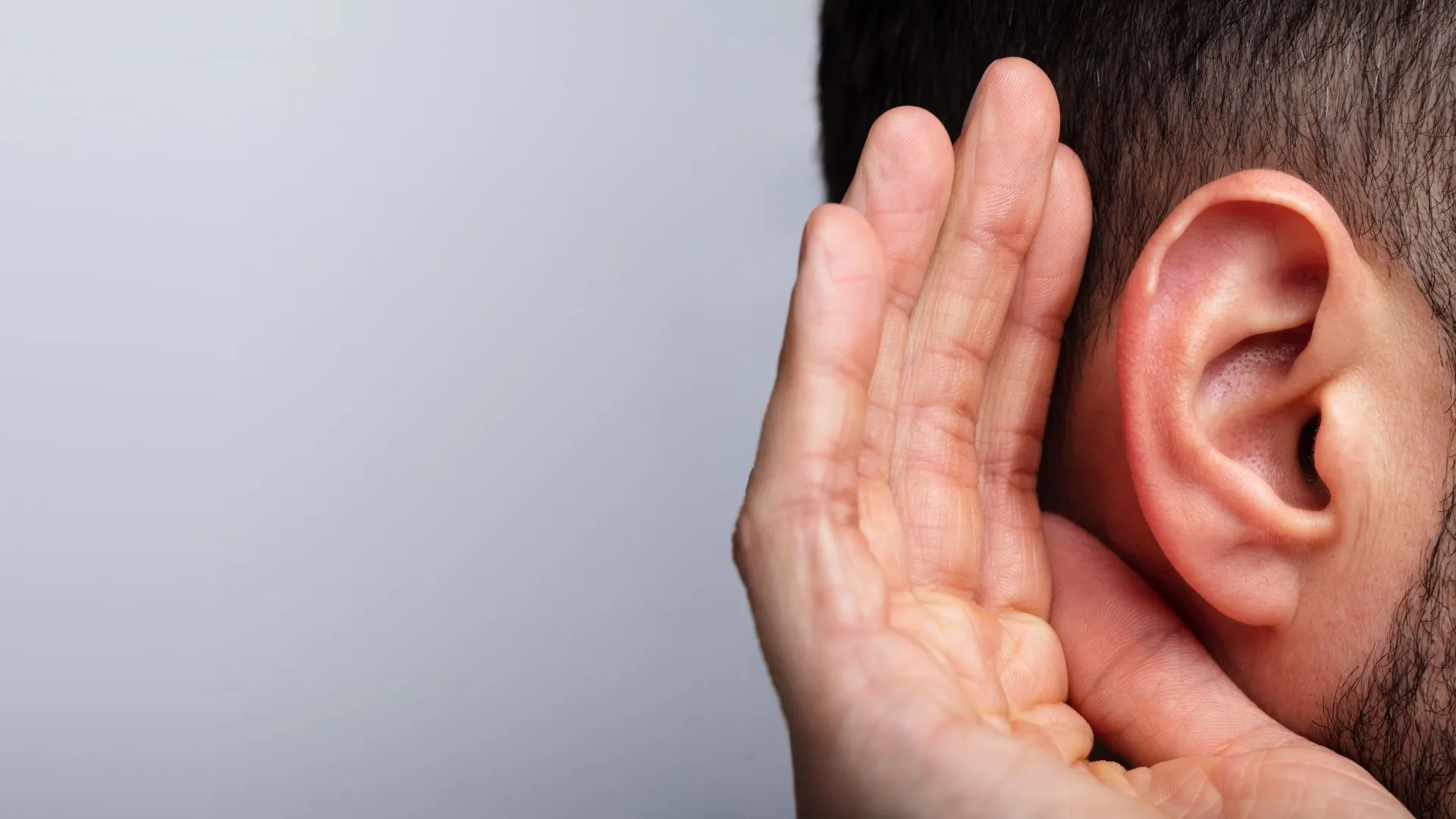A person cupping a hand to their ear, straining to hear